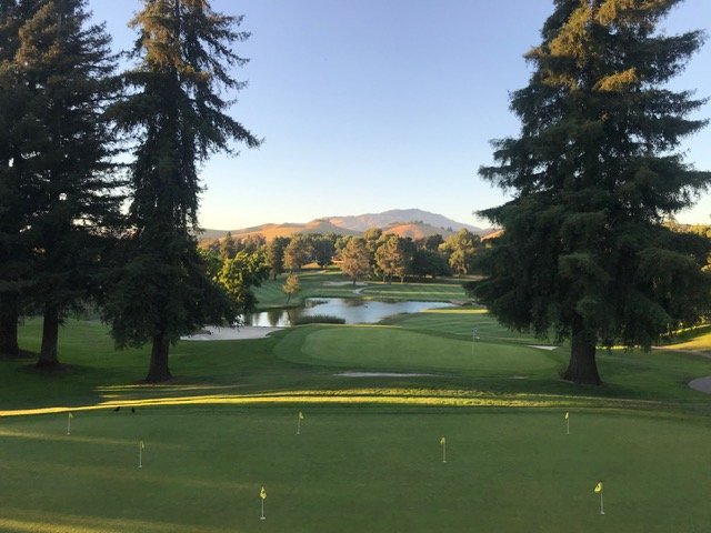 View from the Crow Canyon Country Club clubhouse over the practice green to a pond and Mount Diablo, framed by tall trees